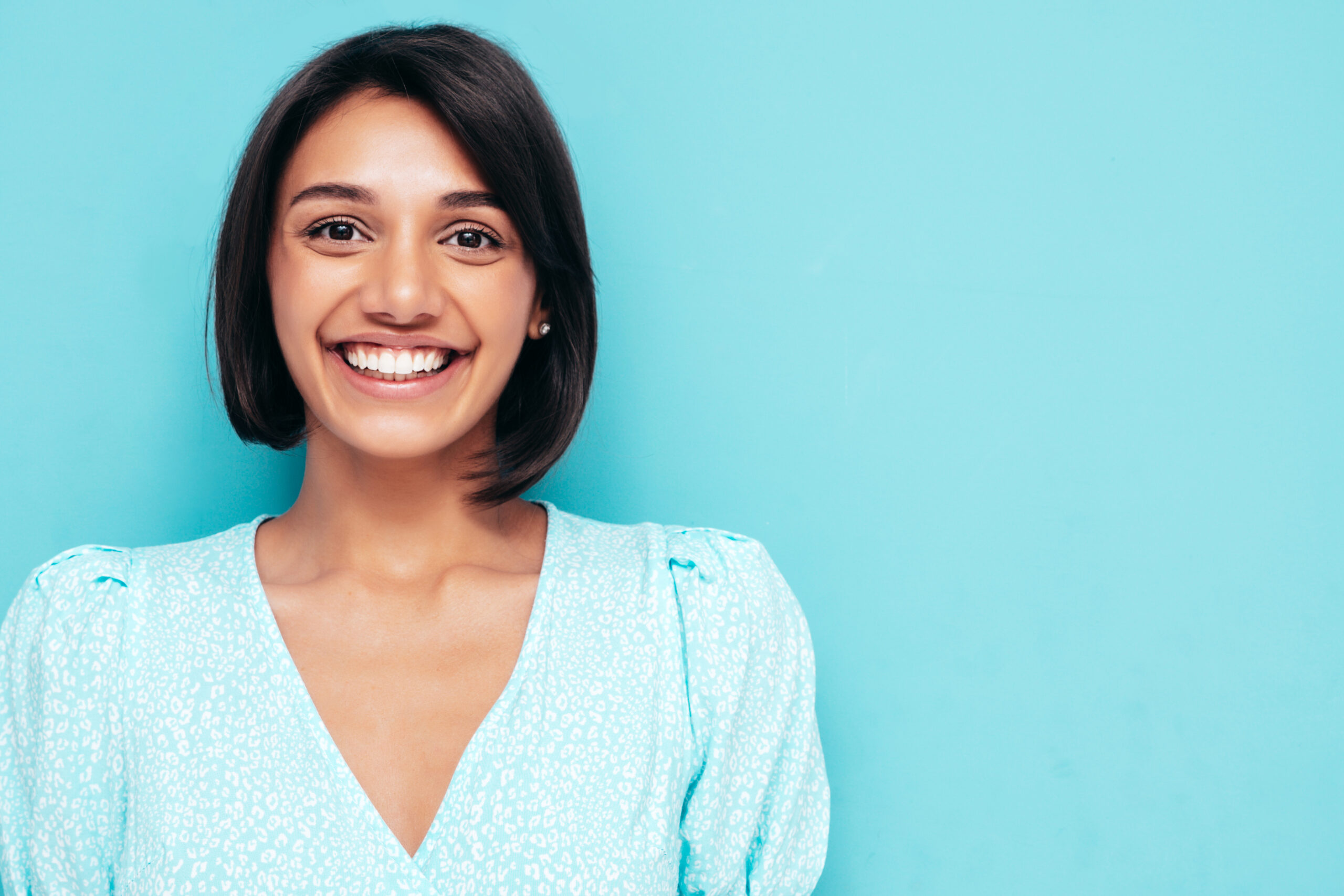 Young beautiful smiling female in trendy summer white dress. Sexy carefree woman posing near blue wall in studio. Positive model having fun. Cheerful and happy. Isolated